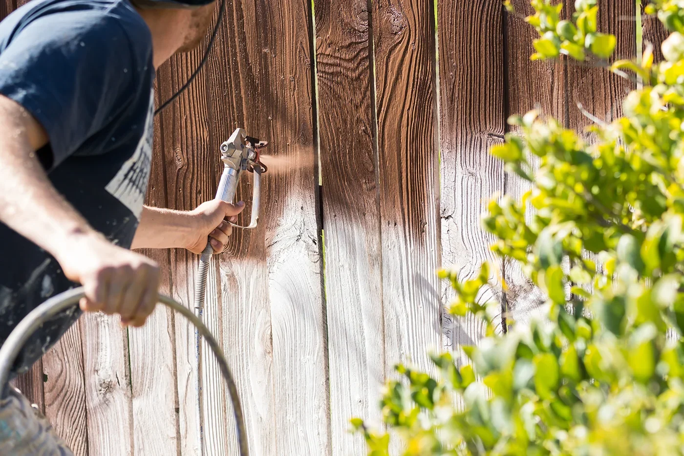 Fence Staining Painter spray staining a weathered wood fence