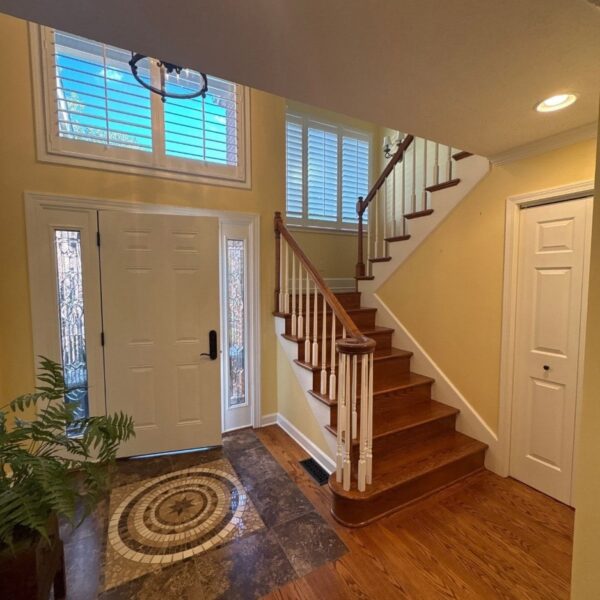 Foyer with yellow walls, white trim and a wood staircase after interior painting