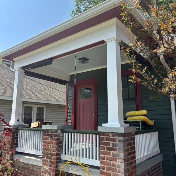 Front porch of a dark green house with a red door, white columns and red trim