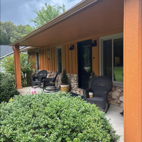 Covered porch of a house painted burnt orange with a black front door
