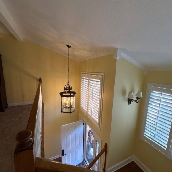 Two story entryway with butter yellow walls, white trim and a lantern pendant light